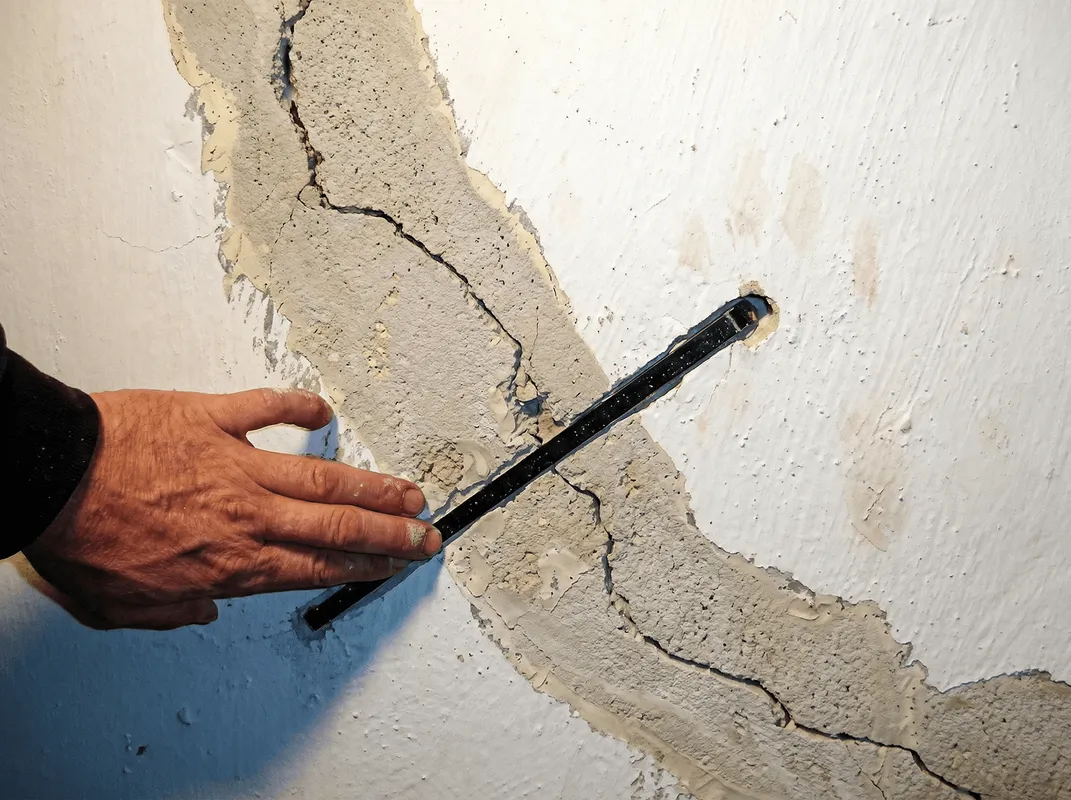 A wall with a large crack is being inspected by a professional in Pittsburgh, PA